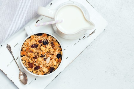Cup of muesli with tropical fruits and white milk jug on wooden board. Concept of healthy eating in pure tonesの写真素材