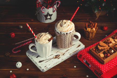 Cozy Christmas composition.Two mug with hot drinks, chocolate with whipped cream and cappuccino with cinnamon stick on a dark wooden background. Sweet treats for cold winter days.の写真素材