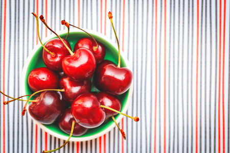 Sweet colorful fresh cherries in a bowl on white textured background, top view with copy spaceの写真素材