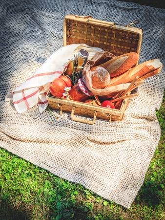 Picnic basket filled with fruit , bread and jar with apricot jam on beige plaid.の写真素材