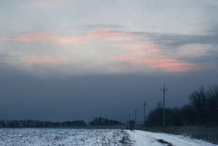 Heavy cloudy sky over the winter field road.の写真素材