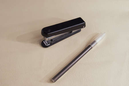Stapler and pen on a white leather texture background