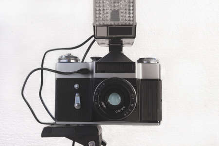 Old Soviet film camera on a tripod with a flash and a lens on a white background.