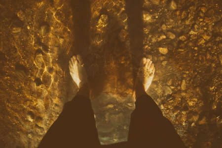 Feet in the water on the rock bottom of the mountain stream, close-up