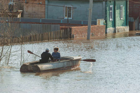 Russia, Balashov April 24, 2018. People in a boat sail along a flooded street to their house. Sunken under water fence street houses property. Flooded during the spring flood of the Hoper River suburbanのeditorial素材