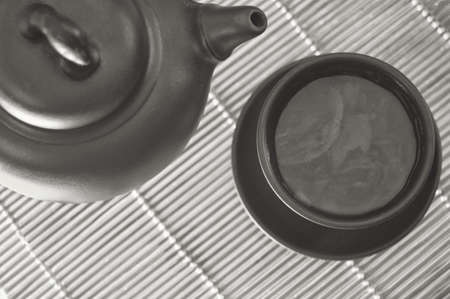 Clay cup and teapot with green tea on a bamboo mat. Composition of a tea ceremony black and white.の写真素材