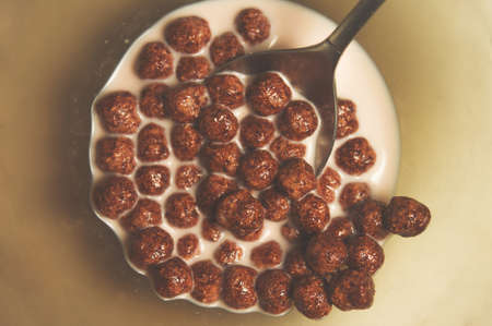 Dry healthy chocolate breakfasts in the form of balls in a plate of milk with a dessert spoon....