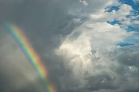 A blue cloudy day sky with beautiful clouds and bright colorfull rainbow for the designer's background.の写真素材