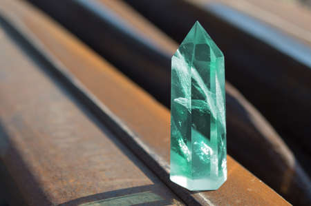 Large transparent mystical faceted crystal of colored green emerald quartz on a rails on industrial background close-up. A wonderful mineral of the royal size for the designer.の写真素材