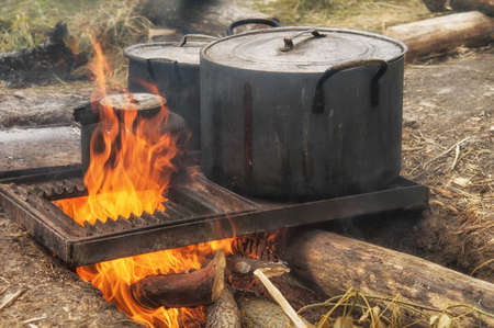 Field kitchen. Saucepan, pot and kettle on fire from the bonfire. Water boils and cooking food in the tourist campaign.の写真素材