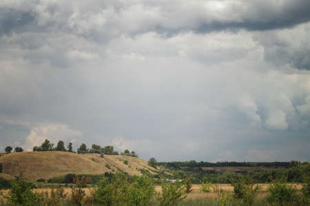 Overcast under the village. Cloudy landscape over pasture meadows in a picturesque hilly summer valleyの写真素材