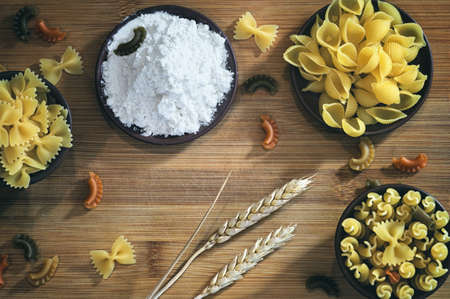 Natural cereal pasta, flour, ears of wheat on a wooden background. Rural kitchen, set products with complex carbohydrateの写真素材