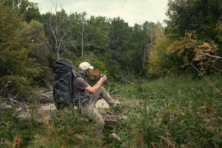 Tourist with large backpack in wilds early autumn photographs nature. Landscape with taiga forest, swamp. Hard hike walkの写真素材