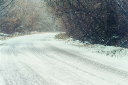 Winter winding road between gray trees in the forests of Russia. Dangerous turn of the road in bad weather in snow and ice.の写真素材