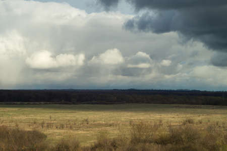 Air view from the hill to the spring pasture valley under a heavy moody cloudy sky. Russian landscape of remote places with yellow blue motiveの写真素材