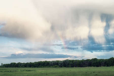 Fluffy clouds and rainbow over the forest. Landscape of spring forested valley and beautiful cloudy skyの写真素材