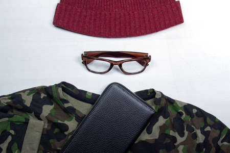On a white background lies a camouflage men's t-shirt, brown glasses and a red men's hatのeditorial素材
