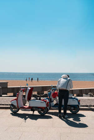 Russia. St. Petersburg. The Gulf of Finland. 300th anniversary park. A guy stands near a scooter, and his friends play beach volleyball. The legendary Vespa. Red and blue italian scootersの写真素材