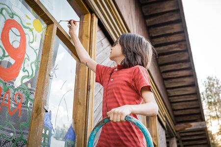 A boy in a red T-shirt draws with colorful gouache on the windowの写真素材