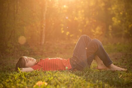 A boy in a red striped t-shirt lies on the grass in the sunshineの写真素材