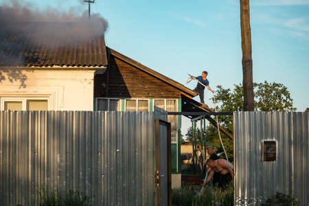 A young man in a blue T-shirt on a roof visor extinguishes a fireのeditorial素材