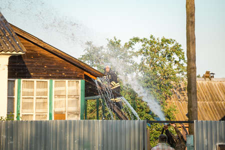 Firefighters in the form of the Ministry of Emergency Situations on the roof extinguish a burning houseのeditorial素材