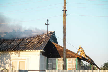 Firefighters in the form of the Ministry of Emergency Situations on the roof extinguish a burning houseのeditorial素材