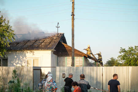 Firefighters in the form of the Ministry of Emergency Situations on the roof extinguish a burning houseのeditorial素材