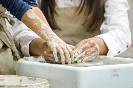 Hands of a little girl who sculpts a craft on a potter's wheel with the help of her motherの写真素材