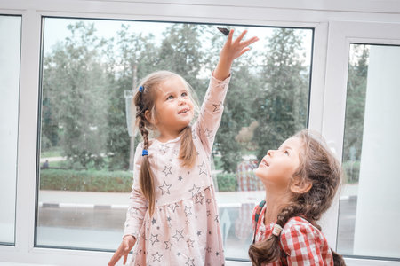 A girl holds a butterfly in her hand, and another girl looks at her.の写真素材