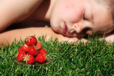 Boy sleeping on grass with pile of ripe strawberries in foreground.の写真素材