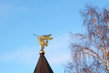 Golden figure of the Archangel with the pipe in the background of sky and treeの写真素材