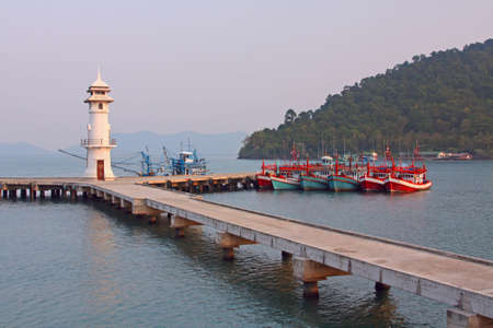 Lighthouse at a pier and fishing boatsの写真素材