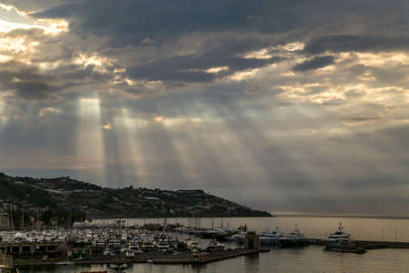Sun rays shining through the clouds  over a port in the Mediterranean sea. Sanremo, Italyの写真素材