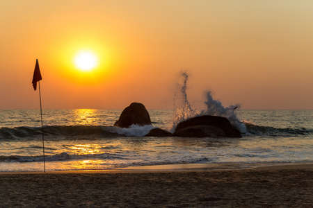 Sunset over the sea. Wave splashing on a rock. Goa, Indiaの写真素材