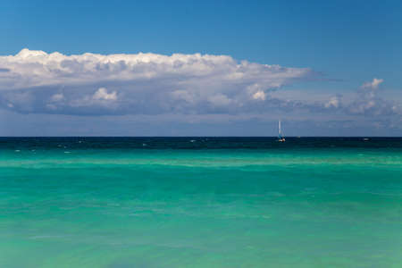 Background of turquoise sea, sky and clouds. Small sailboat at the horizonの写真素材