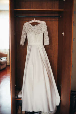 Beautiful white cream wedding dresses made of silk chiffon, tulle and lace hanging on hangers with bowsの写真素材
