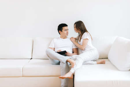 Portrait of smiling cheerful young man and woman hug on white living room background looking at each other. Happy couple embrace laughing having fun together. Good relationships conceptの写真素材