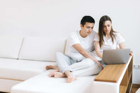 Young serious couple is calculating domestic bills online, managing finances or taxes with laptop application and papers. Young clients customers reviewing bank accounts and planning budget expensesの写真素材