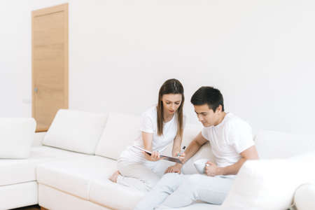 Girl asks guy to sign document. Couple of guy and girl is sitting on sofa are getting ready for their wedding. Young woman and man are preparing for journey.の写真素材