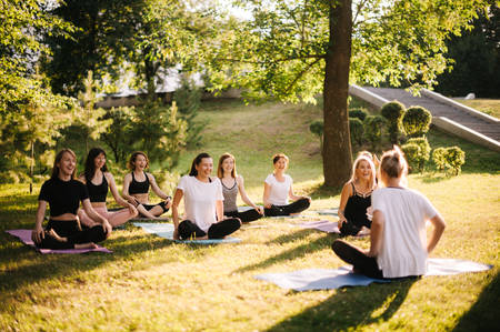 Group of smiling women prepare to meditation in park on summer sunny morningの写真素材