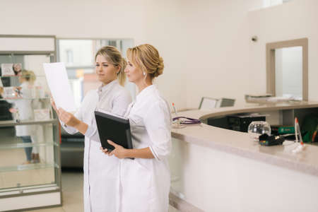 Two woman doctors are looking at the results of the medical tests. Two doctors standing by counter and looking at document in the hospitalの写真素材