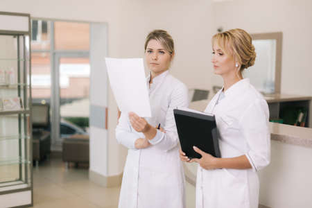 Two medical professionals woman doctor talking in the corridor hospital. Two beautiful female healthcare workers checking the patient papers in hospitalの写真素材