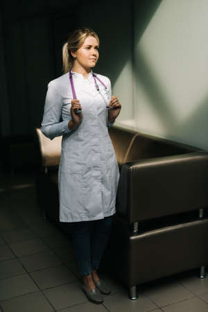 Portrait of young woman doctor wearing white uniform standing in hospital corridor. Female medical nurse or practitioner with stethoscope. Healthcare conceptの写真素材