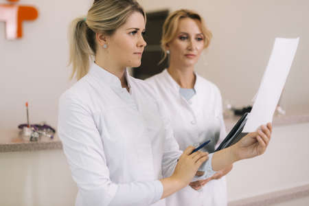 Medical consultation of two professional woman doctors by counter and looking at document in the hospitalの写真素材