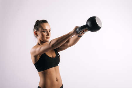 Portrait of muscular sexy young woman in black sportswear is swinging kettlebell on isolated white background.の写真素材