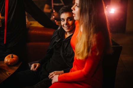 Young man in a Halloween zombie costume looks at a beautiful girl in a red dress tightening her body.の写真素材
