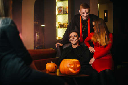 Group of four friends are celebrating Halloween in a cafe. Guys dressed as scary holiday monsters. Carved pumpkin on table.の写真素材