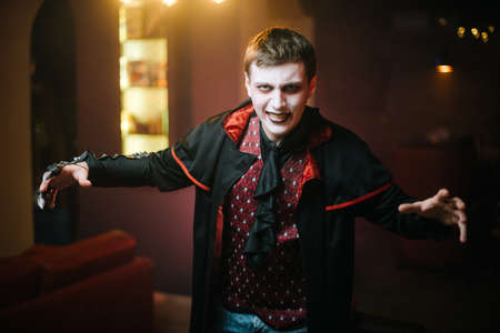 The young man in the Halloween costume of Count Dracula looks ominously at the camera. The guy spread his armsの写真素材
