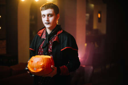 Young man in a Halloween costume of Count Dracula holding a carved pumpkin and loooking at the cameraの写真素材